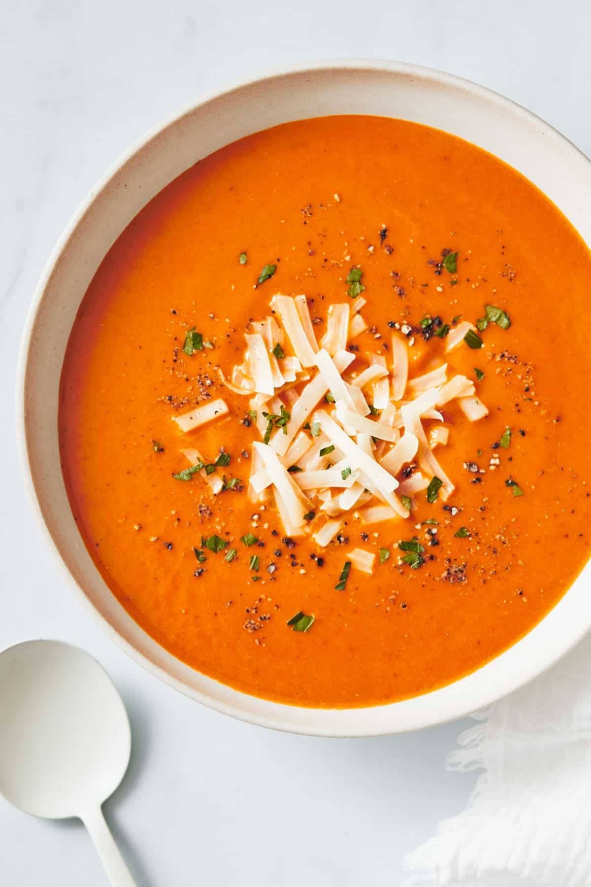 Tomato soup in a bowl in a white bowl with a white spoon.