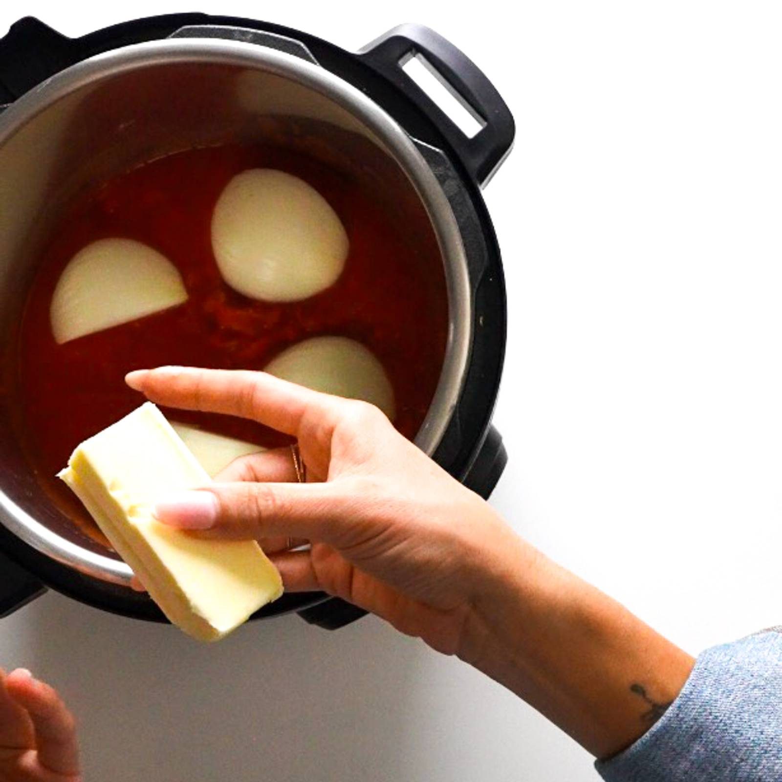 Adding stick of butter to Instant Pot with onions in tomatoes.